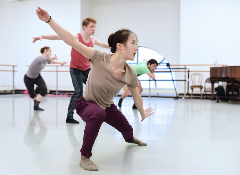 Yin Yue in a deep lunge while dancers behind her learn her steps in a white studio
